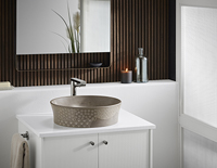 Decorative brown bathroom sink on top of a bathroom cabinet with a mirror above it.